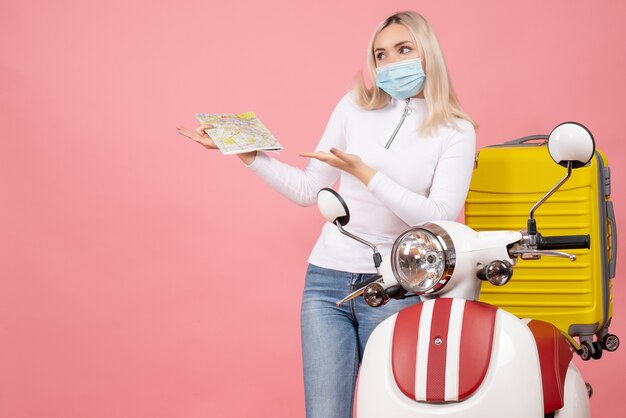 Vue de face jeune femme pointant sur la carte debout près de cyclomoteur