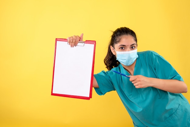 Photo gratuite vue de face de la jeune femme pointant sur le presse-papiers tenant le stylo sur le mur jaune