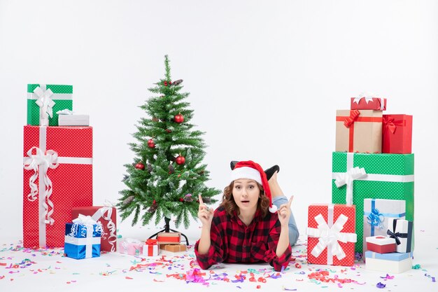 Vue de face de la jeune femme portant autour des cadeaux de Noël et petit arbre de vacances sur le mur blanc