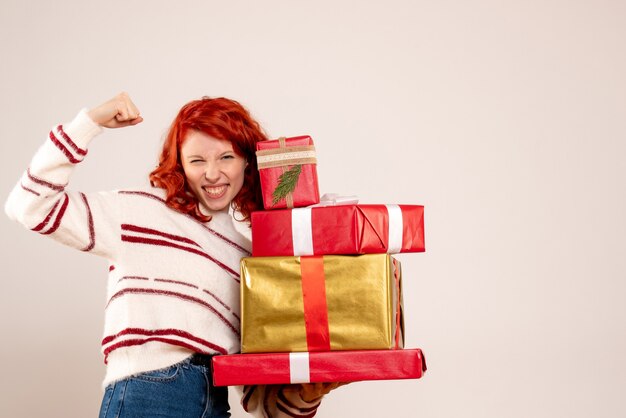 Vue de face de la jeune femme portant des cadeaux de Noël sur un mur blanc