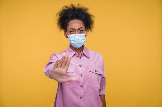 Vue de face d'une jeune femme portant un masque médical et montrant un arrêt avec sa main