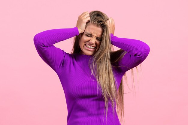 Vue de face d'une jeune femme posant dans une belle robe violette sur le mur rose