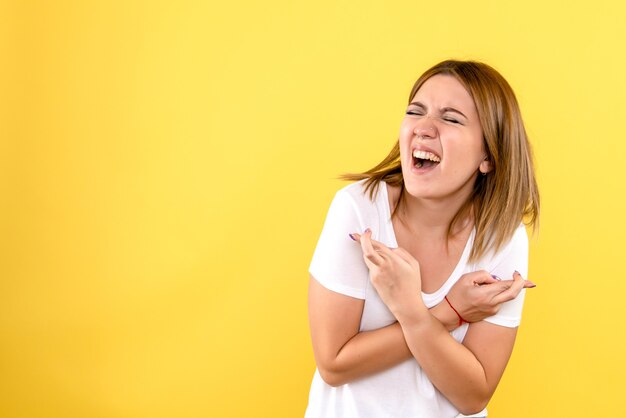 Vue de face de la jeune femme posant émotionnellement sur le mur jaune