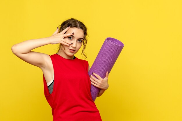 Vue de face de la jeune femme posant avec tapis violet sur mur jaune