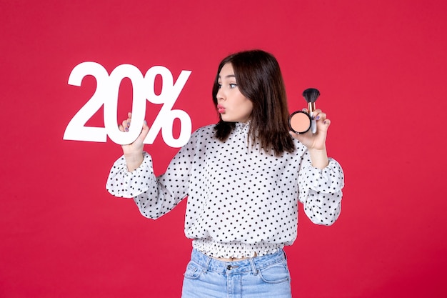 Photo gratuite vue de face jeune femme avec de la poudre de gland pour le maquillage et l'écriture sur le mur rouge