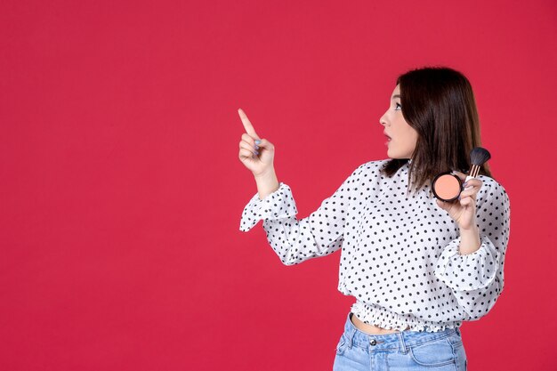 Vue de face jeune femme avec de la poudre de gland pour le maquillage et sur le mur rouge