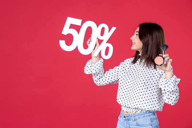 Vue de face jeune femme avec de la poudre de gland pour le maquillage et sur le mur rouge