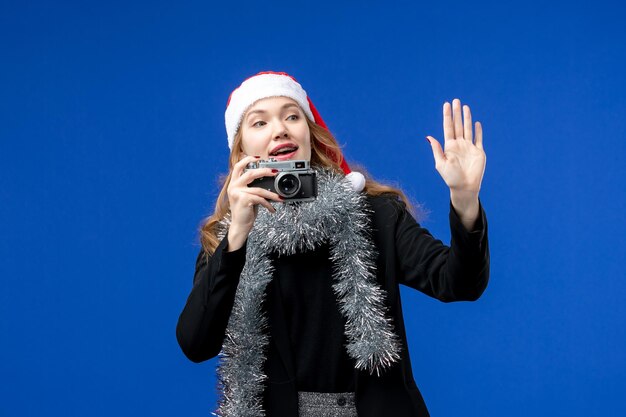 Vue de face d'une jeune femme prenant une photo avec un appareil photo sur un mur bleu