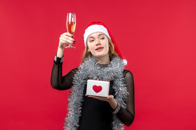 Vue de face jeune femme avec présent célébrant sur le mur rouge couleur vacances Noël