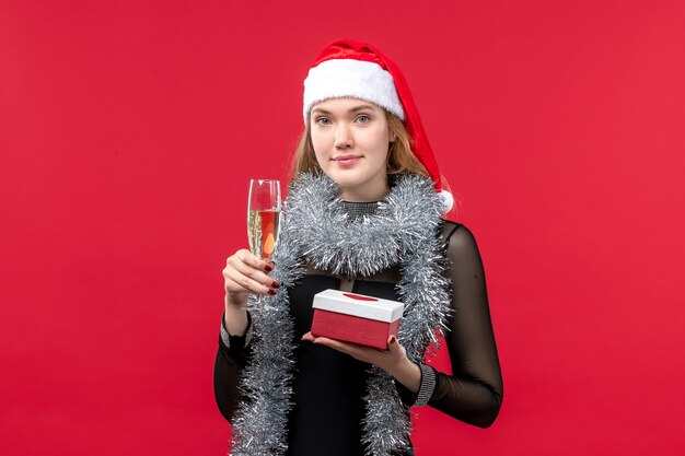 Vue de face jeune femme avec présent célébrant sur le mur rouge vacances couleur de Noël