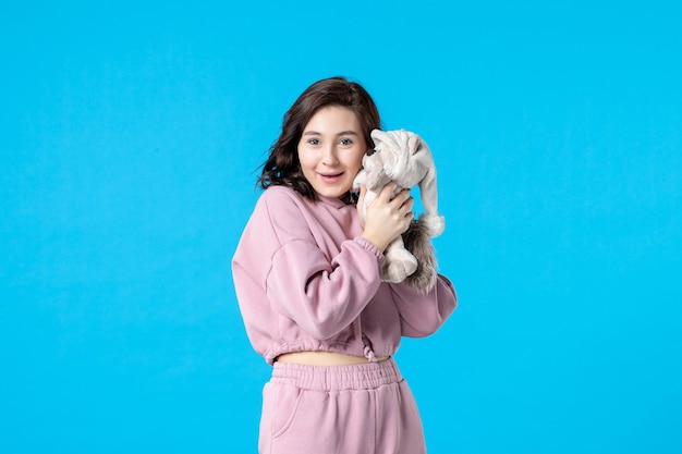 Vue de face jeune femme en pyjama rose avec petit ours en peluche sur bleu