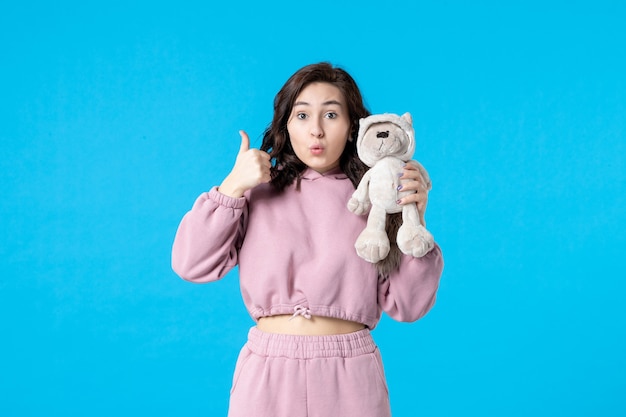 Vue de face jeune femme en pyjama rose avec petit ours en peluche de couleur bleue