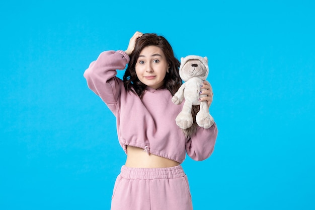 Vue de face jeune femme en pyjama rose avec petit ours en peluche sur couleur de rêve bleu nuit sommeil insomnie repos fête de lit