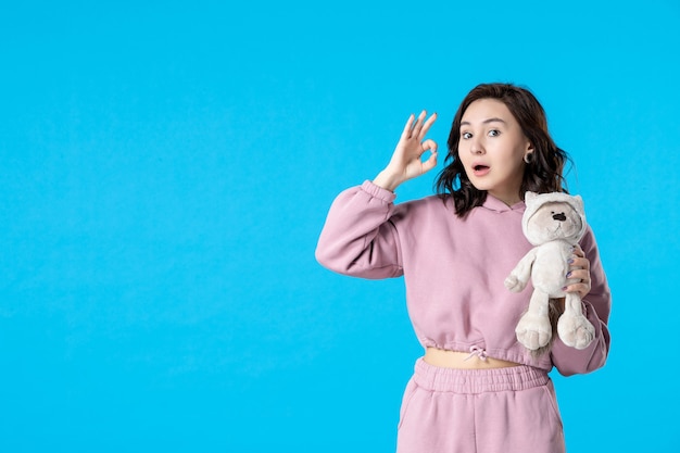 Vue de face jeune femme en pyjama rose avec petit ours en peluche sur la couleur de rêve bluesleep