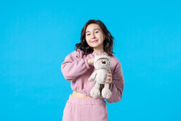 Vue de face jeune femme en pyjama rose avec petit ours en peluche sur des couleurs de rêve bleu nuit sommeil lit femme fête reste insomnie