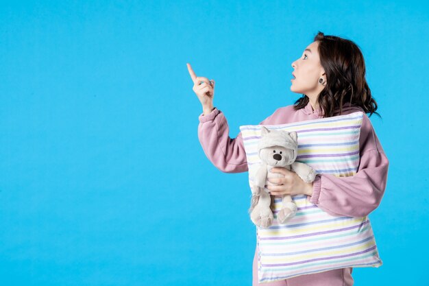 Vue de face jeune femme en pyjama rose avec petit ours en peluche et oreiller sur femme bleue