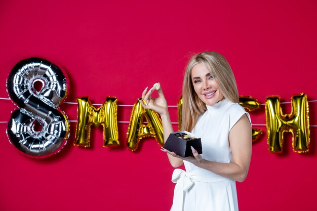 Vue de face jeune femme en robe blanche posant avec de délicieux bonbons le jour de la femme rouge décorée