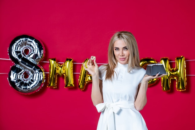 Photo gratuite vue de face jeune femme en robe blanche posant avec de délicieux bonbons sur une photo rouge décorée de la journée des femmes