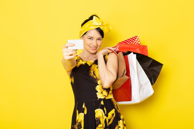 Une vue de face jeune femme en robe de fleur jaune-noir conçu avec un bandage jaune sur la tête tenant des colis sur le jaune