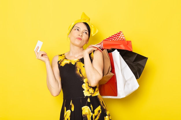 Une vue de face jeune femme en robe de fleur jaune-noir conçu avec un bandage jaune sur la tête tenant des colis sur le jaune