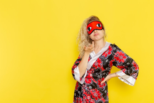 Vue de face jeune femme en robe de nuit et portant un masque pour les yeux se préparant à dormir posant sur un mur jaune nuit sommeil couleur de l'obscurité féminine