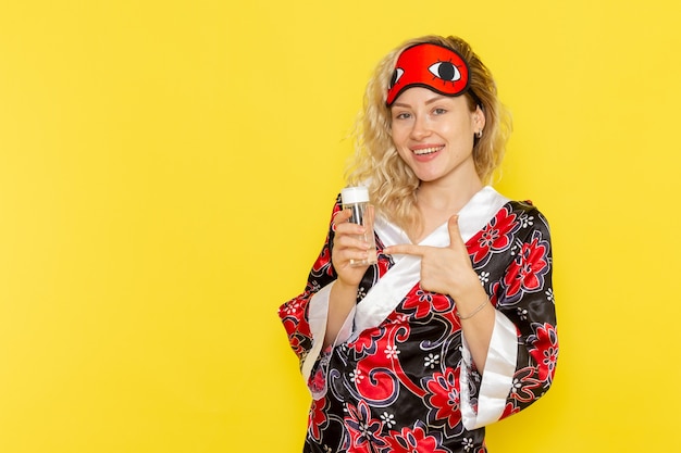 Vue de face jeune femme en robe de nuit et portant un masque pour les yeux se préparant à dormir tenant le ballon sur le mur jaune sommeil modèle féminin lit de nuit