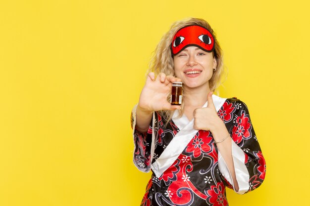 Vue de face jeune femme en robe de nuit et portant un masque pour les yeux se préparant à dormir tenant des pilules sur le mur jaune sommeil nuit modèle femme obscurité