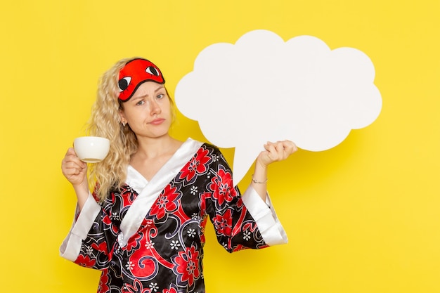 Vue De Face Jeune Femme En Robe De Nuit Tenant Un énorme Panneau Blanc Et Boire Du Café Sur Le Mur Jaune Sommeil Nuit Couleur Modèle De Lit