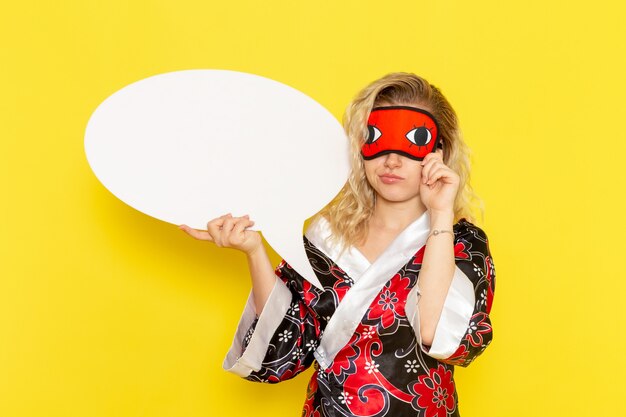 Vue de face jeune femme en robe de nuit tenant un énorme panneau blanc sur mur jaune sommeil nuit modèle de lit fille couleur