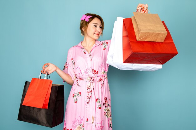 Une vue de face jeune femme en robe rose conçue de fleurs tenant des paquets d'achat et souriant sur bleu