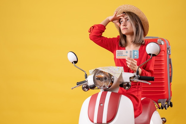 Vue de face jeune femme en robe rouge tenant un billet regardant quelque chose sur un cyclomoteur