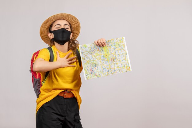 Vue de face jeune femme avec sac à dos brandissant la carte mettant la main sur sa poitrine