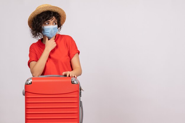 Vue de face jeune femme avec sac en masque sur fond blanc virus covid- voyage de couleur de vacances de pandémie de soleil touristique