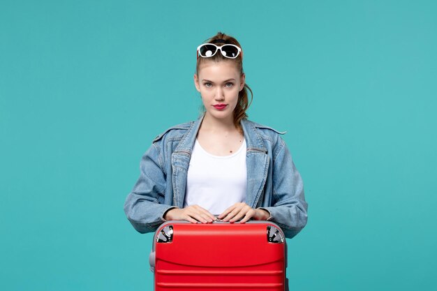 Vue de face jeune femme avec sac de préparation pour les vacances sur l'espace bleu clair