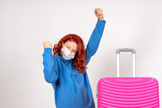 Vue de face de la jeune femme avec sac rose en masque se réjouissant sur mur blanc