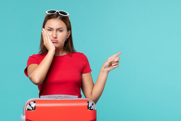 Vue de face jeune femme avec sac rouge se préparant pour les vacances sur le bureau bleu