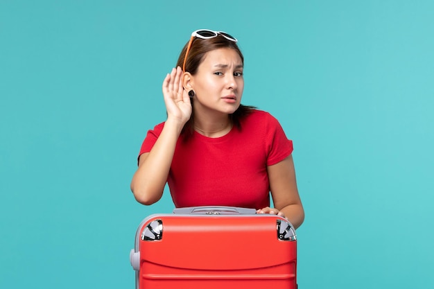 Vue de face jeune femme avec sac rouge se préparant pour les vacances en essayant d'entendre sur l'espace bleu