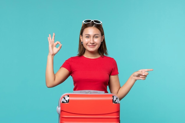 Vue de face jeune femme avec sac rouge se préparant pour les vacances en souriant sur l'espace bleu