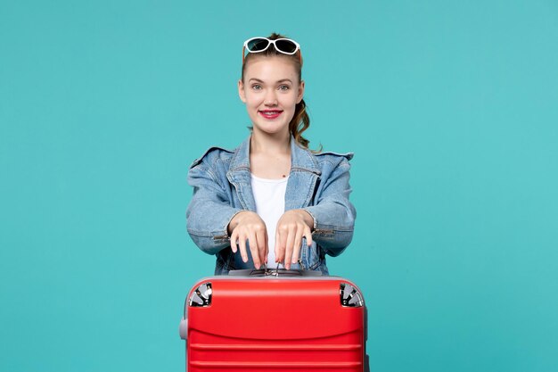 Vue de face jeune femme avec sac rouge se préparant pour les vacances en souriant sur l'espace bleu