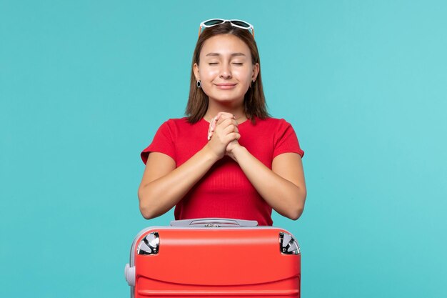 Vue de face jeune femme avec sac rouge se préparant pour les vacances en souriant sur l'espace bleu