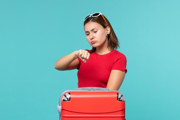 Vue de face jeune femme avec sac rouge se préparant pour les vacances vérifier le temps sur l'espace bleu