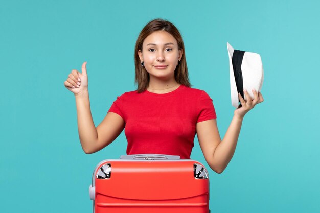 Vue de face jeune femme avec sac rouge tenant son chapeau sur l'espace bleu clair