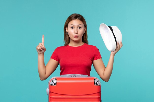 Vue de face jeune femme avec sac rouge tenant son chapeau sur l'espace bleu