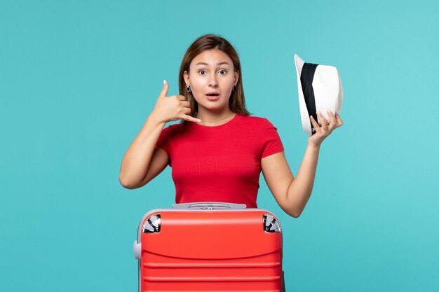 Vue de face jeune femme avec sac rouge tenant son chapeau sur l'espace bleu