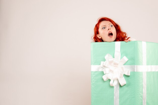 Vue De Face De La Jeune Femme Se Cachant à L'intérieur Du Cadeau De Noël Sur Le Mur Blanc