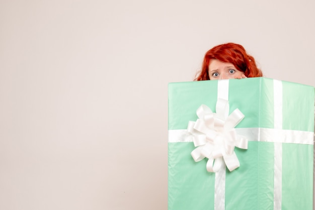Vue de face de la jeune femme se cachant à l'intérieur du cadeau de Noël sur le mur blanc