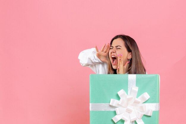 Vue de face jeune femme se cachant à l'intérieur présent et criant sur fond rose