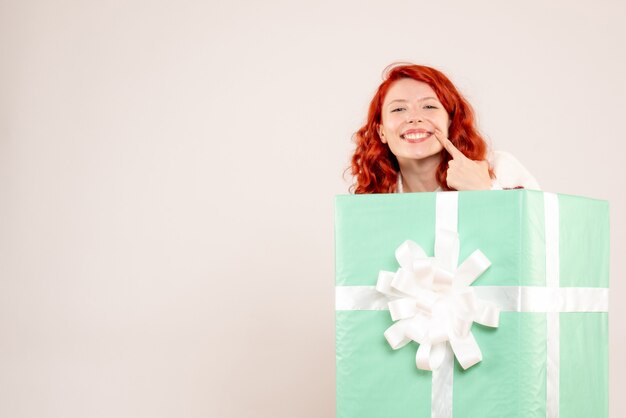 Vue de face de la jeune femme se cachant à l'intérieur présent souriant sur mur blanc