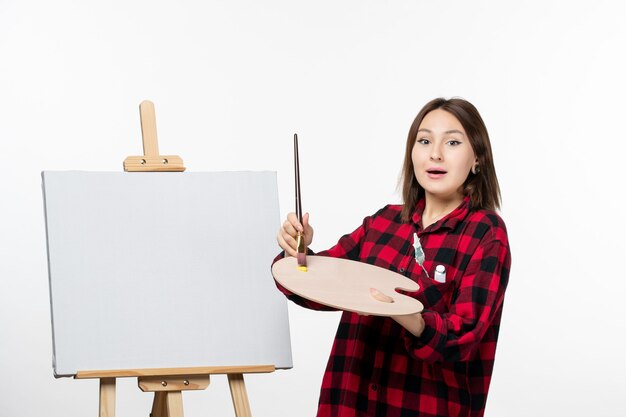 Vue de face jeune femme se préparant à peindre sur un chevalet sur un mur blanc