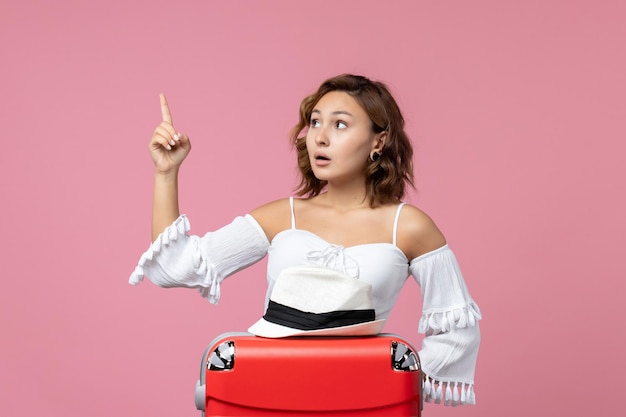 Vue de face d'une jeune femme se préparant pour des vacances avec un sac et posant sur le mur rose